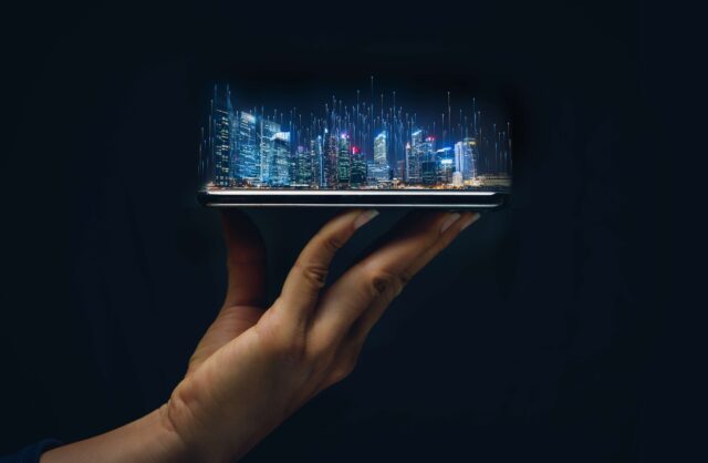 Eine Hand hält ein Tablet, auf dem sich ein Hologramm einer digitalen Stadt befindet