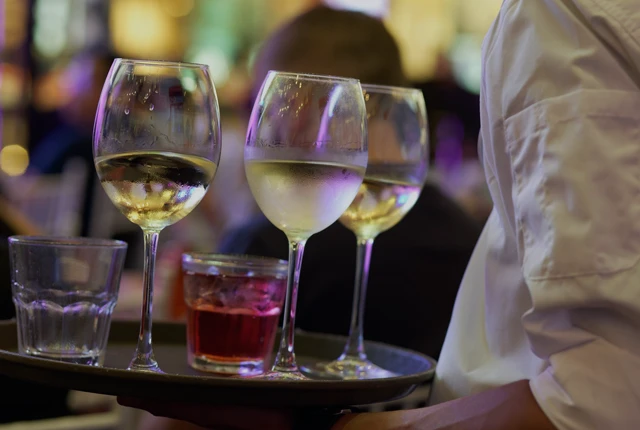 Ein Kellner trägt ein Tablett mit drei Weingläser und zwei Wassergläser.